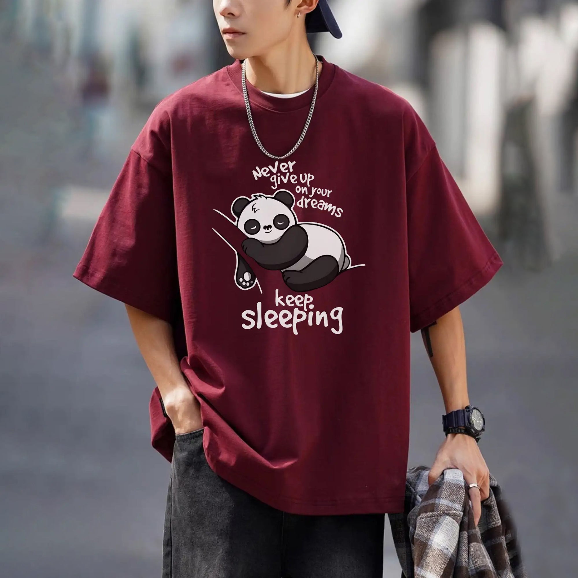 Person wearing a maroon t-shirt with a panda graphic and text, standing outdoors.